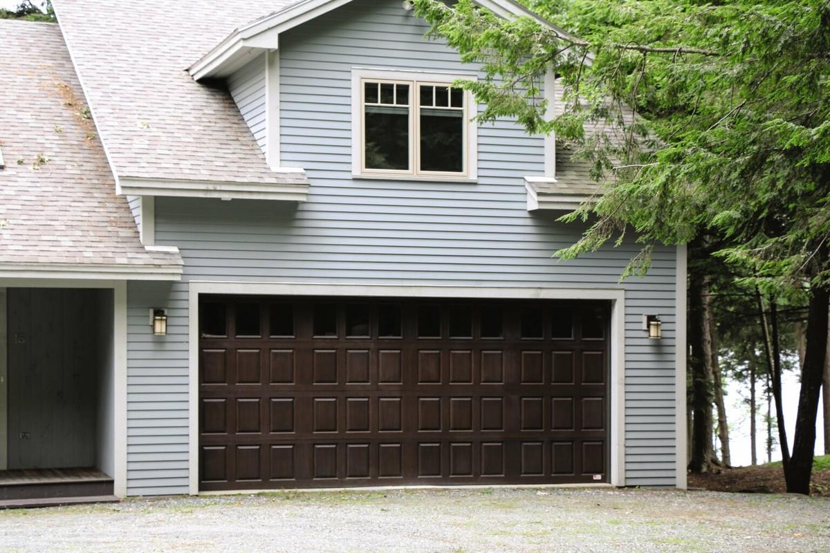 A light blue house with a sturdy brown garage door, showcasing what to consider when buying a garage door.